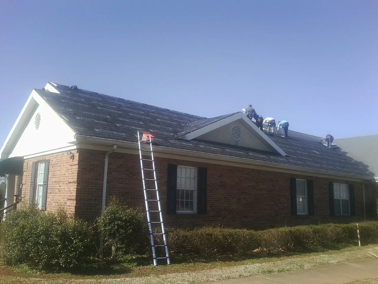Crew tearing shingles off a brick ranch roof with a ladder set — Metal Roof Repair work by our crew in Alameda