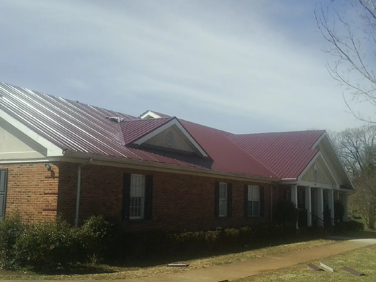 Red metal roof with gabled entries on a long brick building, from a Hail Damage Roof Repair job in Alameda