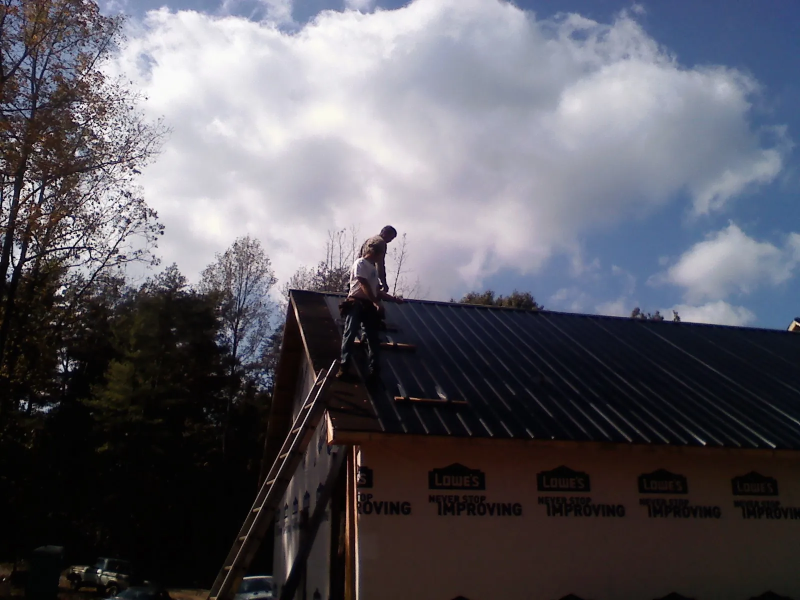 Roofer fastening dark metal panels high against a cloudy sky, from a Roof Inspection job in Alameda
