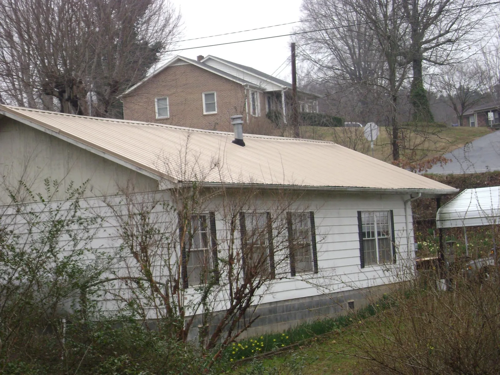 Tan metal roof on a white sided house set into a hillside — Commercial Roofing by Roofing Brothers in Alameda